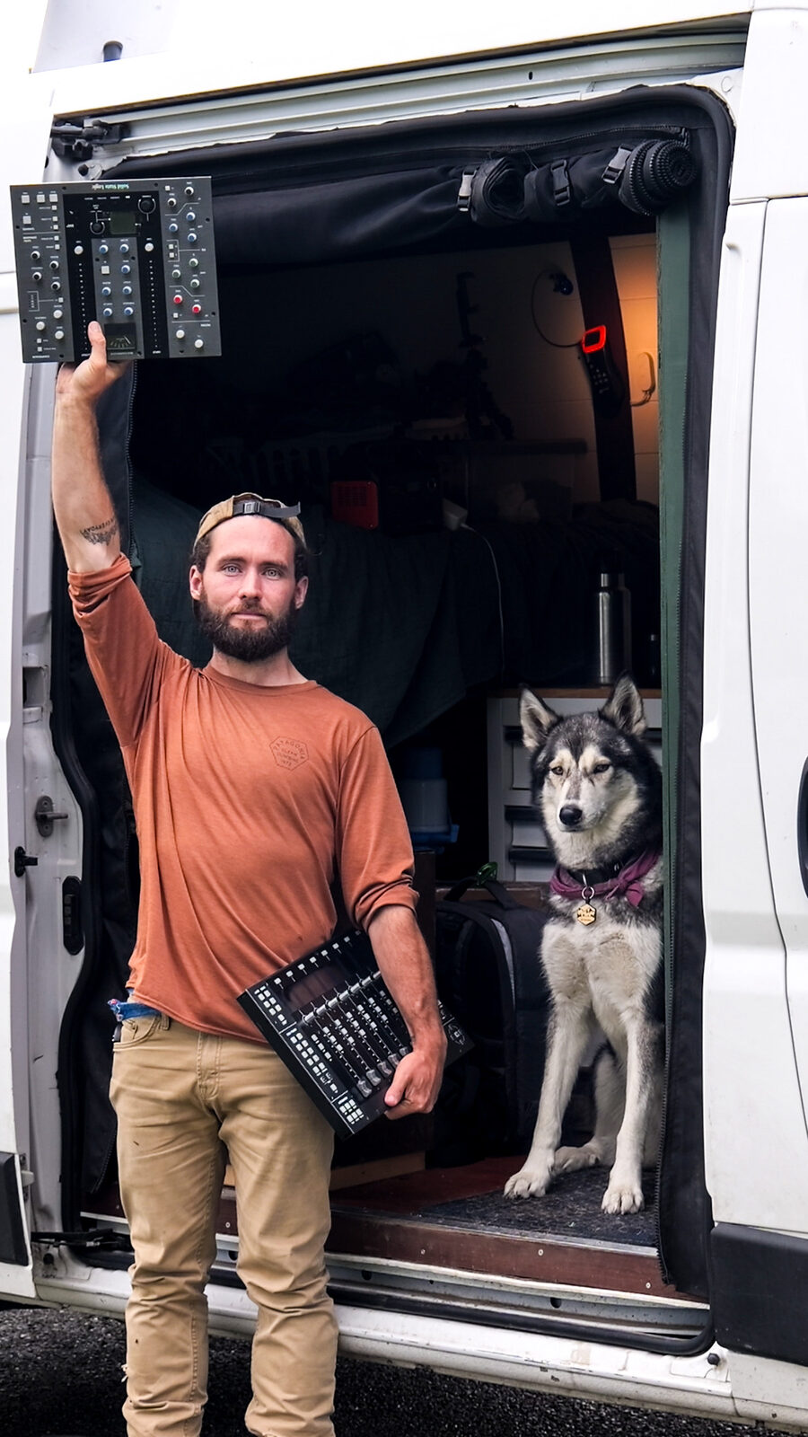 Josh holding mixing gear at the van door with Margo the husky
